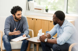 The mid adult male client listens as the young adult male therapist repeats what he just heard.